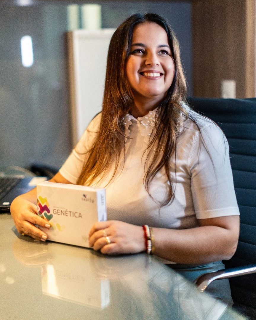 Dra. Ana Cristina no consultório, segurando o kit do teste genético